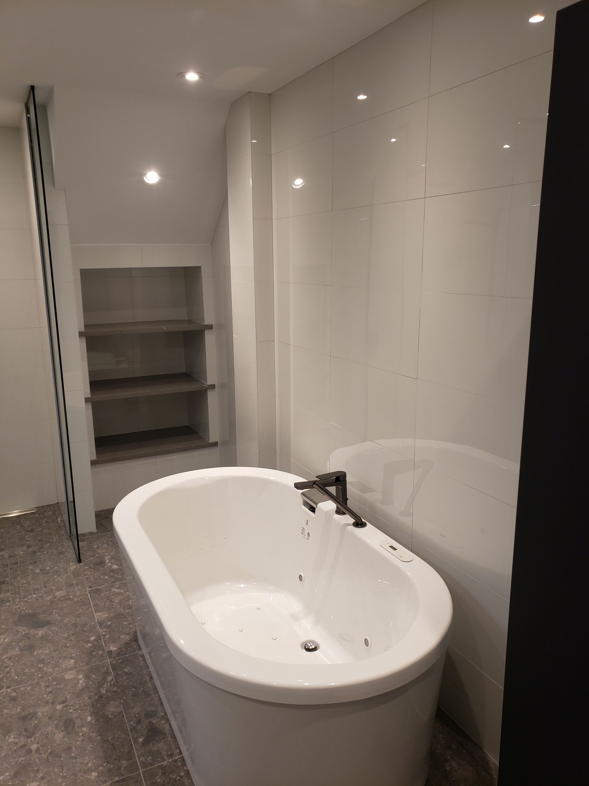 Salle de bains moderne avec baignoire ovale blanche, étagères intégrées et murs carrelés blancs.