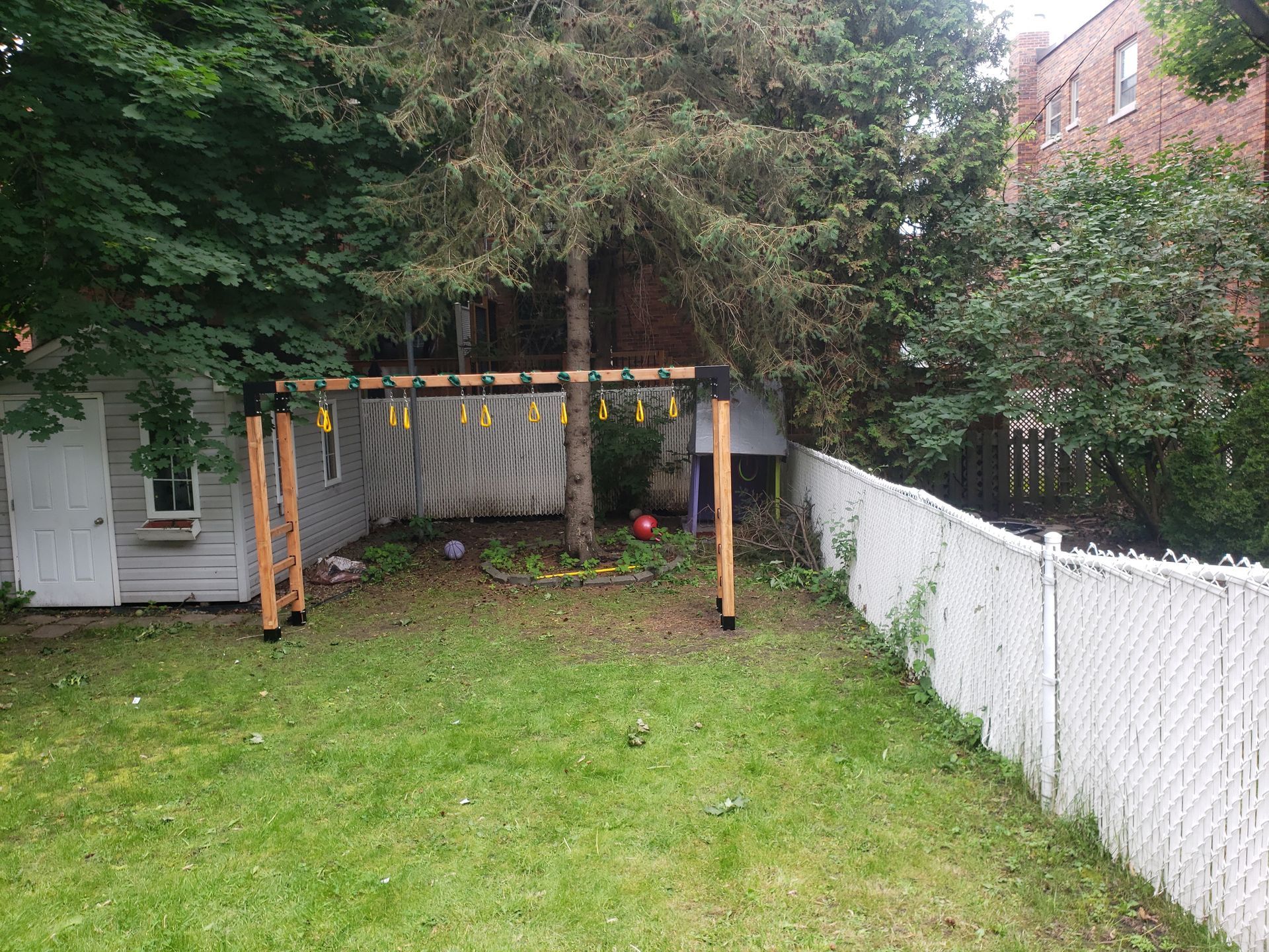 Cour arrière avec balançoire, pelouse, arbres, clôture blanche et petit bâtiment.