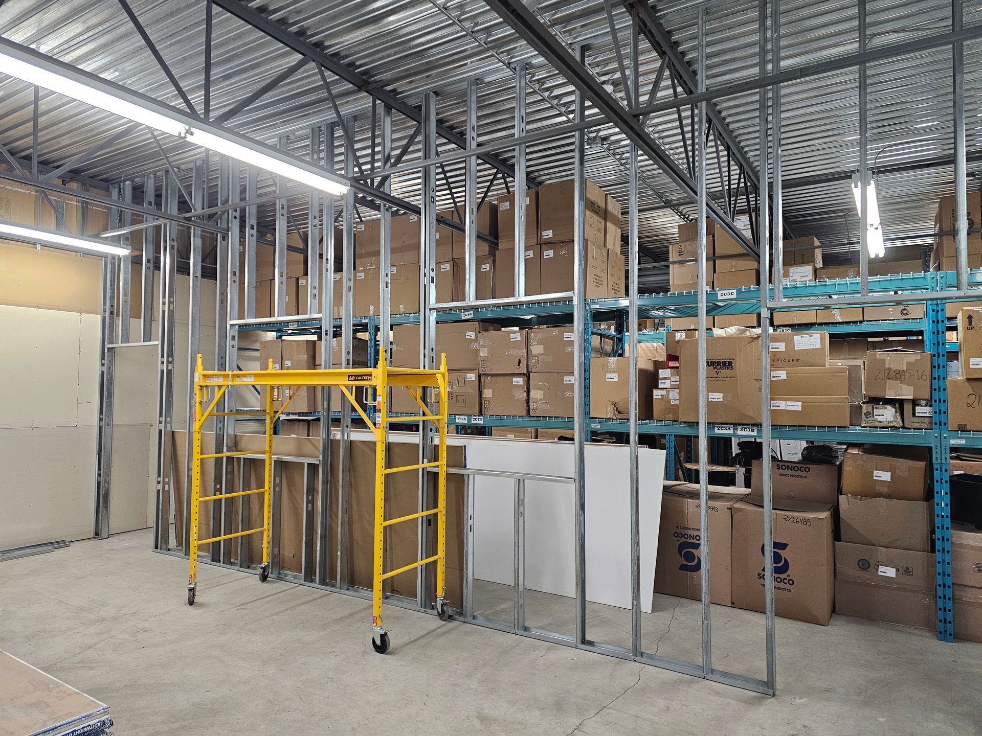 Intérieur d'entrepôt avec des montants métalliques pour les murs, des échafaudages jaunes et des cartons sur des étagères.