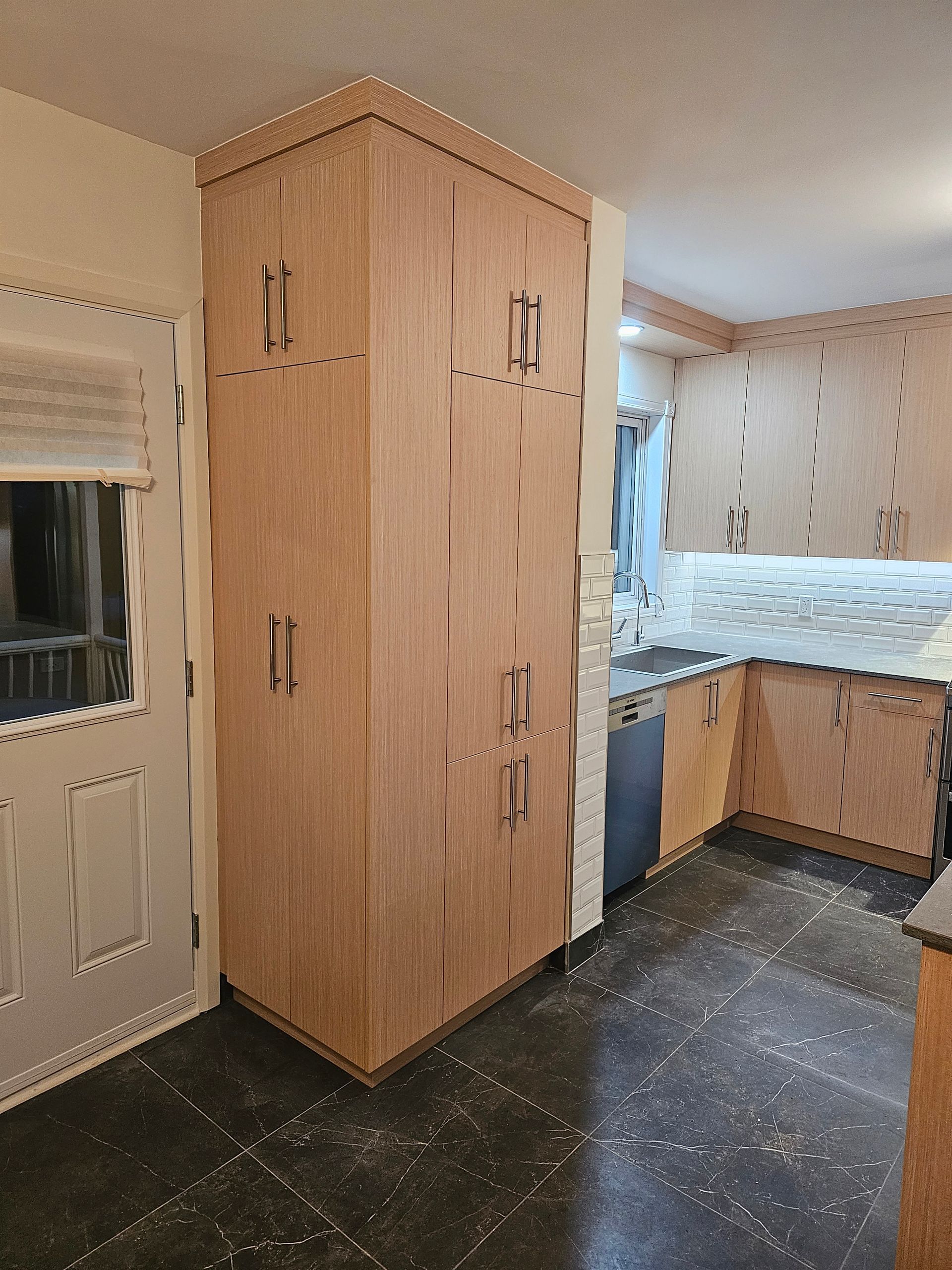 De hauts placards de cuisine en bois sont placés à côté d'une porte, dans une cuisine au sol foncé.