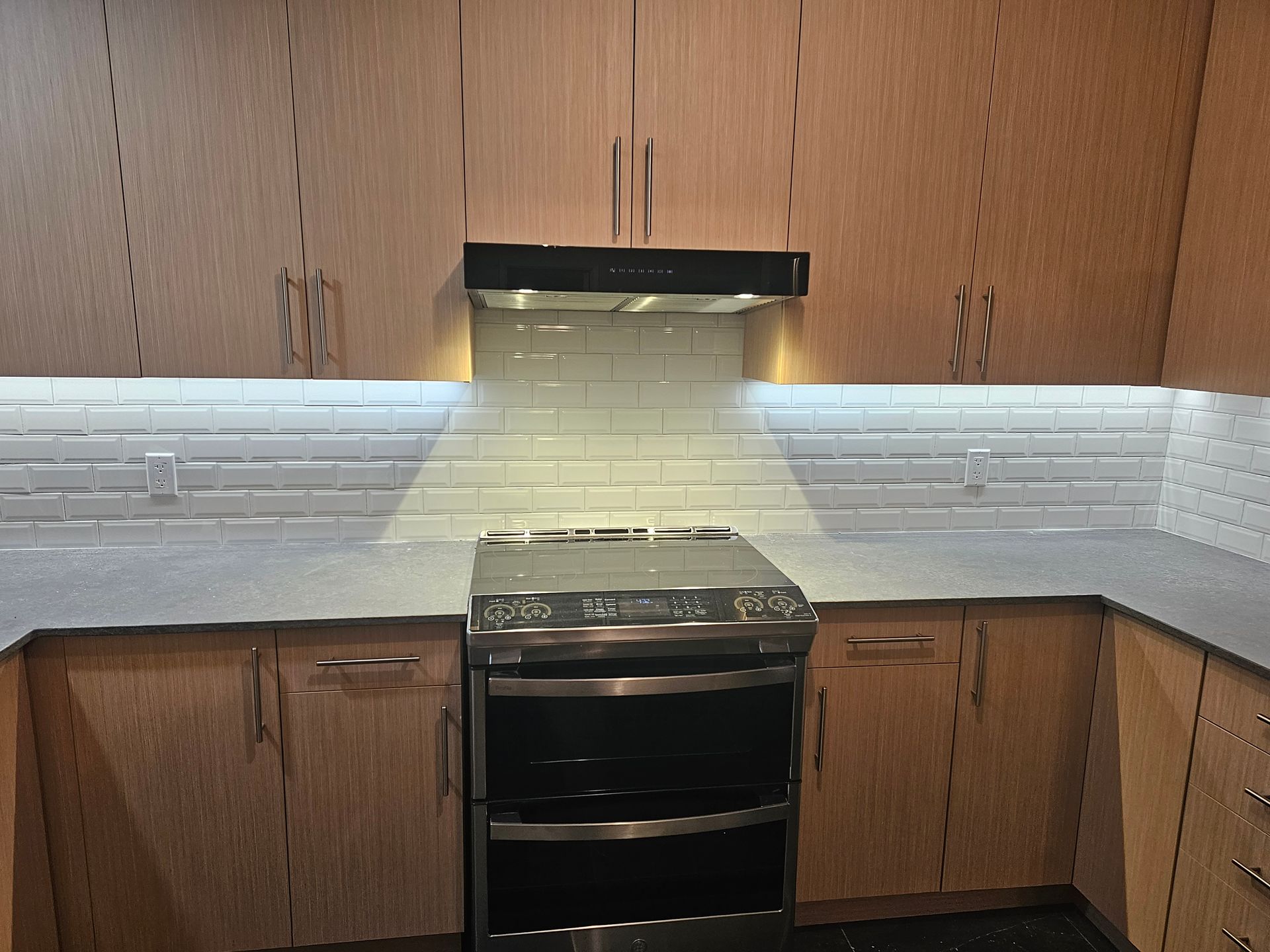 Cuisine avec armoires en bois clair, comptoir gris, crédence en carreaux de métro blancs et cuisinière en acier inoxydable.