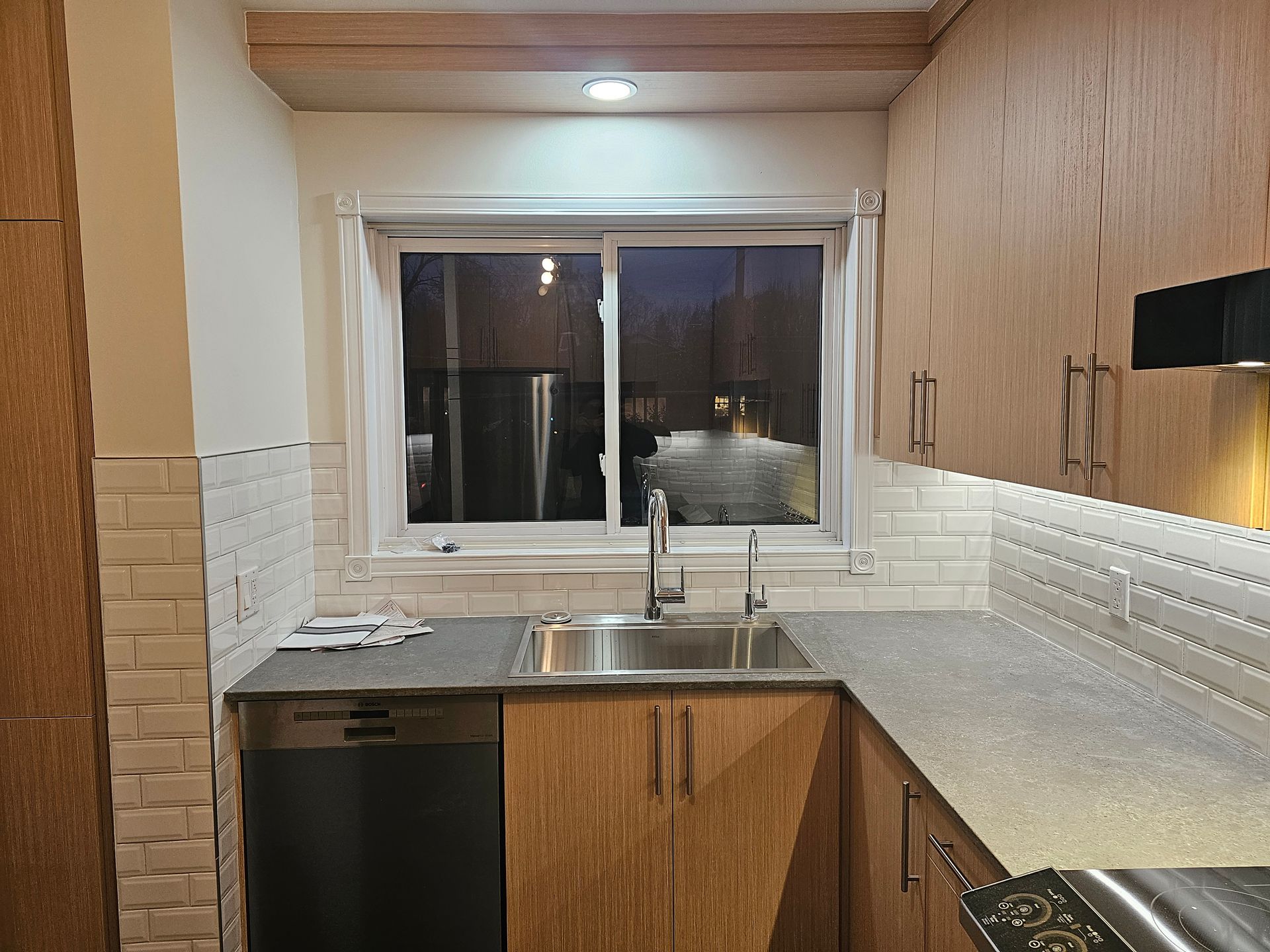 Cuisine avec placards en bois, un évier et une fenêtre donnant sur un paysage extérieur sombre.