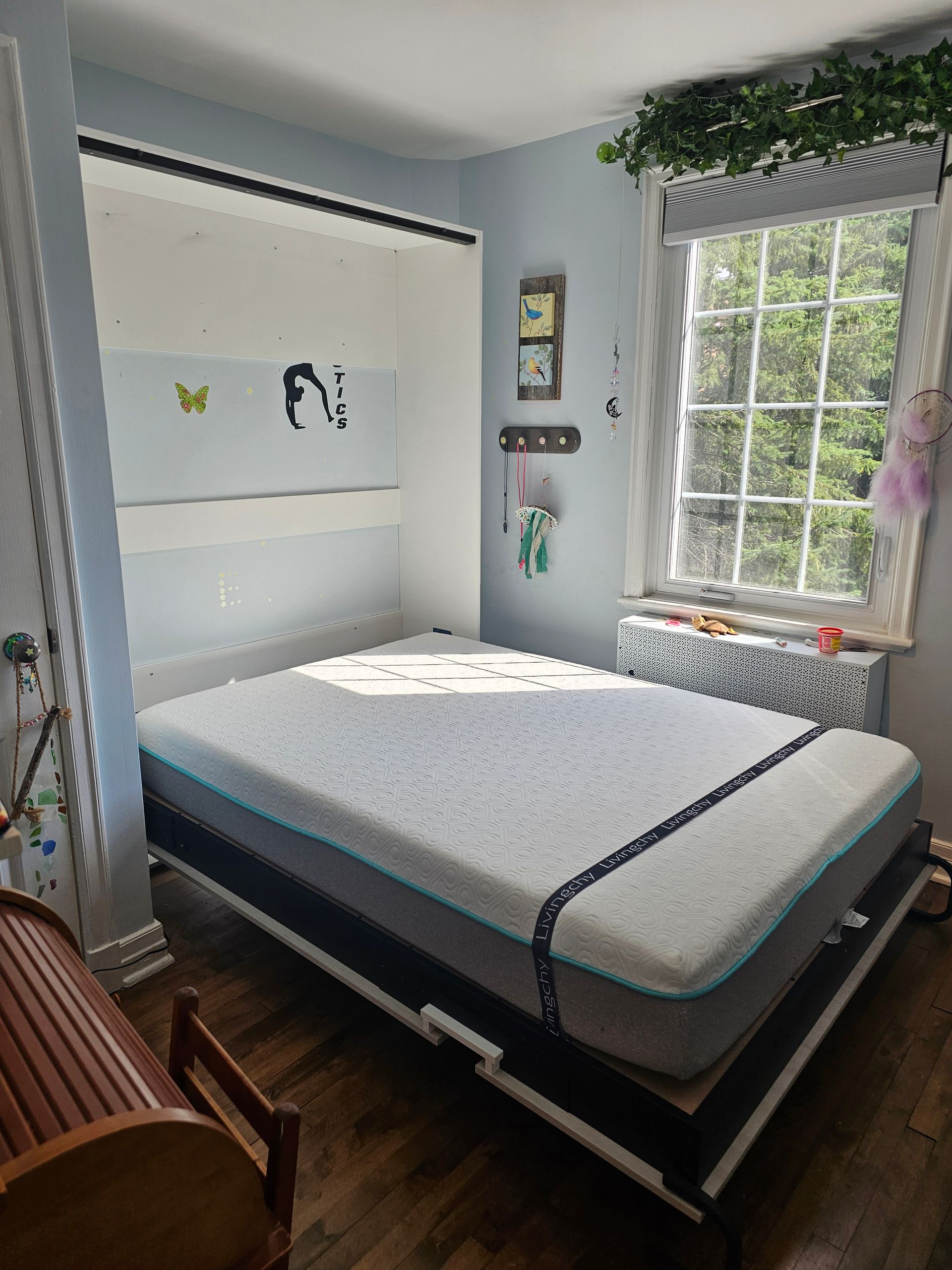 Chambre avec un lit, une fenêtre et une armoire murale. Murs bleu clair, lumière du soleil sur le lit.