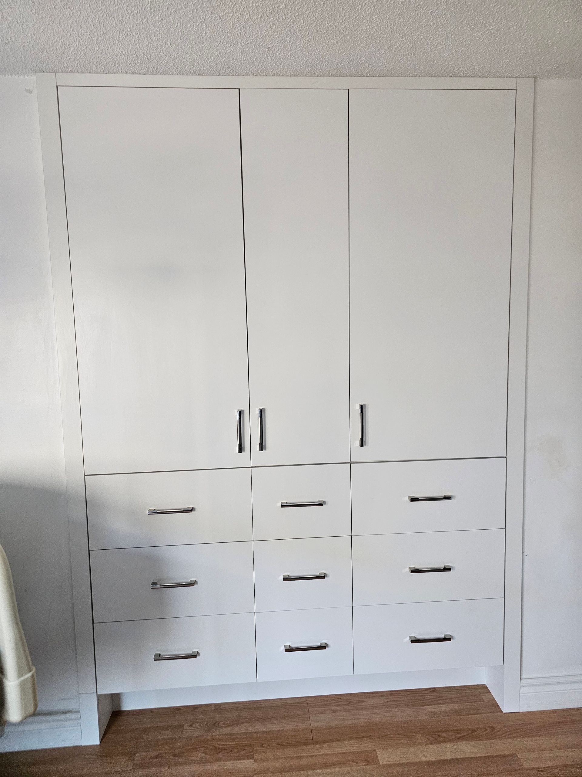 Armoire encastrée blanche avec trois portes supérieures, six tiroirs inférieurs ; poignées argentées.