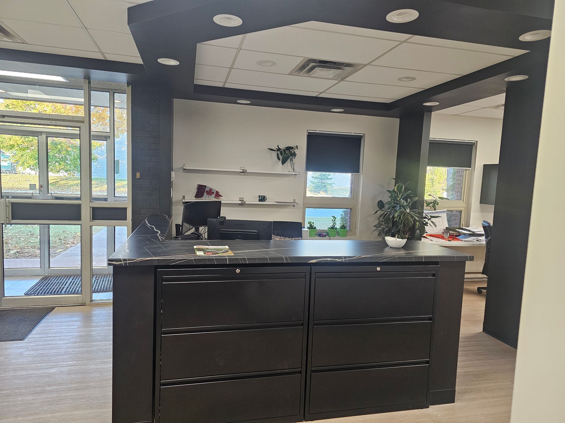 Espace d'accueil avec comptoir et armoires sombres, porte ouverte et fenêtres, avec un plafond au design noir et blanc.