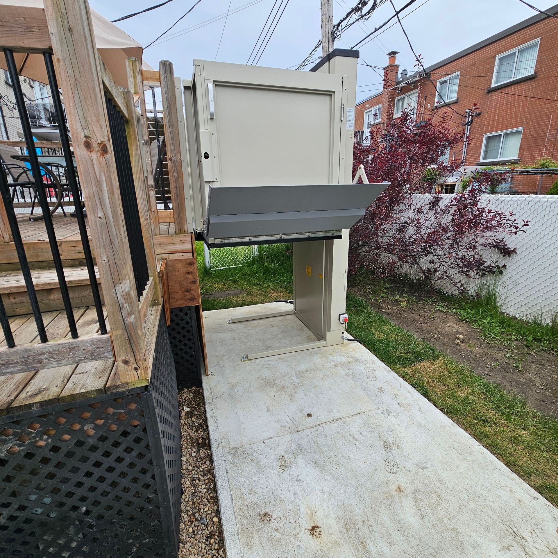 Ascenseur extérieur pour fauteuils roulants à côté d'une terrasse en bois, avec une rampe en béton.