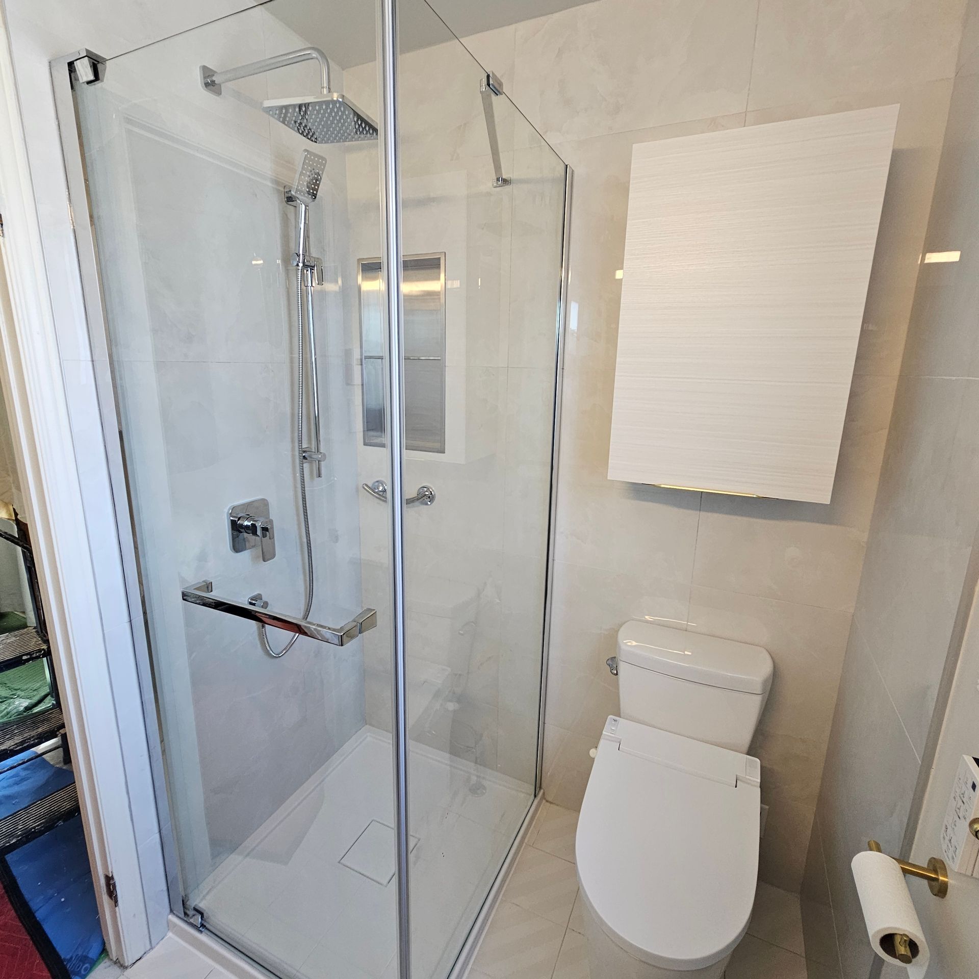 Salle de bains avec douche en verre, toilettes et murs carrelés de blanc. Une armoire murale est fixée au-dessus des toilettes.
