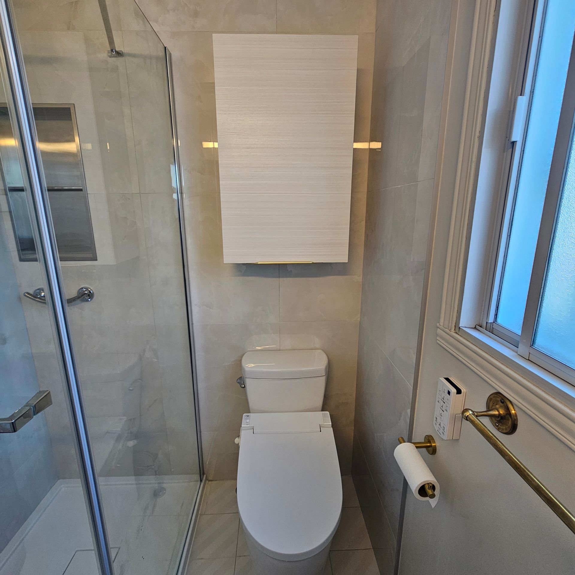 Salle de bains avec toilettes blanches, douche en verre et porte-serviettes doré avec une serviette blanche.