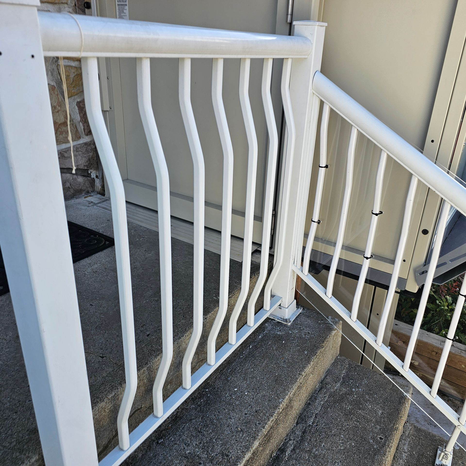 Rambardes et balustres en métal blanc sur des marches en béton menant à une porte.