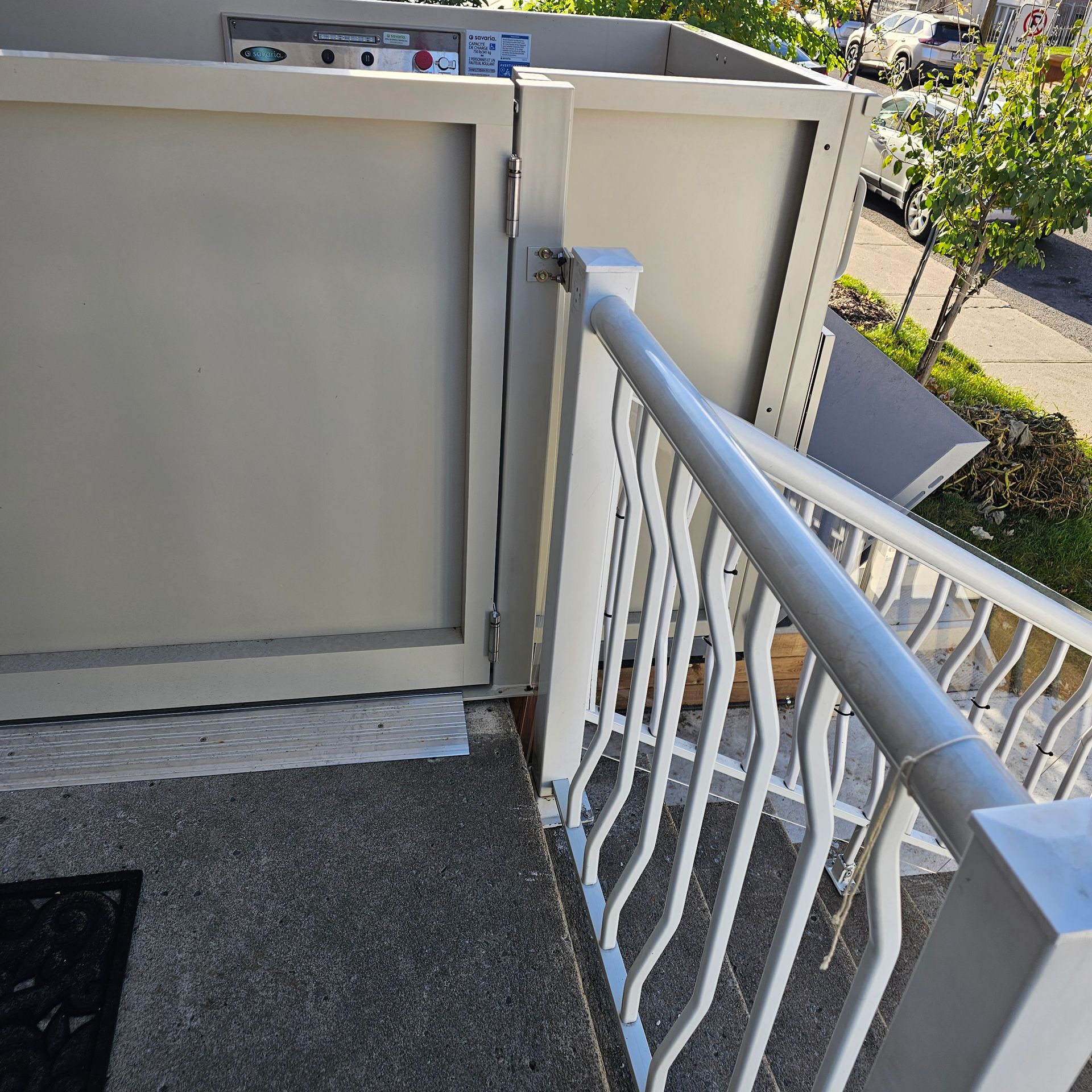 Balcon extérieur avec panneaux métalliques gris clair et rambarde blanche ; des marches en béton y mènent.