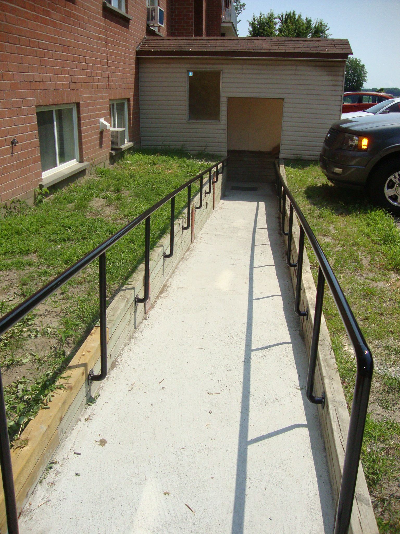 Rampe en béton avec mains courantes noires menant à l'entrée d'un bâtiment.