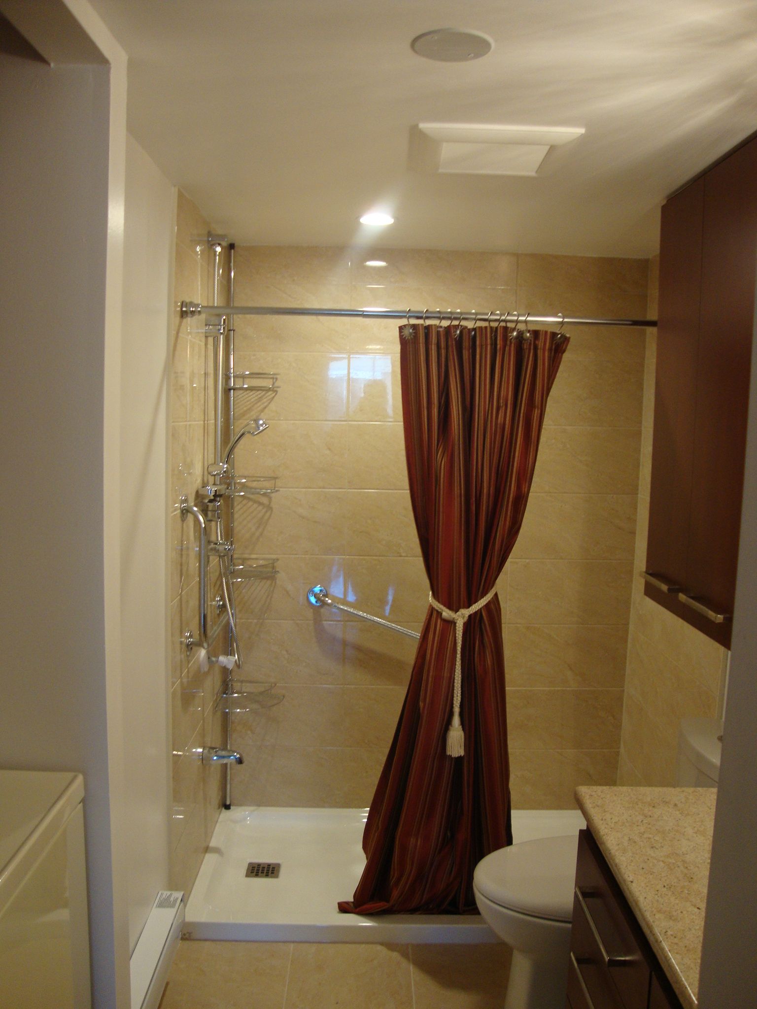 Petite salle de bains avec douche et rideau ; carrelage beige, rideau marron, robinetterie blanche.