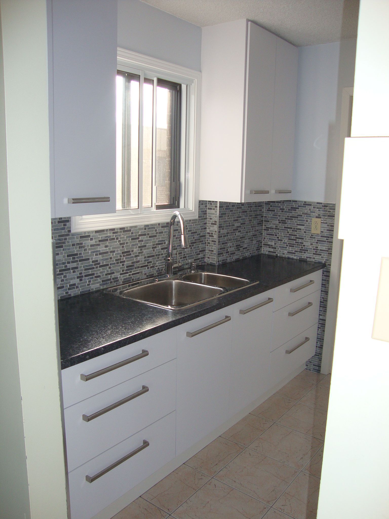 Petite cuisine moderne avec placards blancs, plans de travail foncés et crédence carrelée.