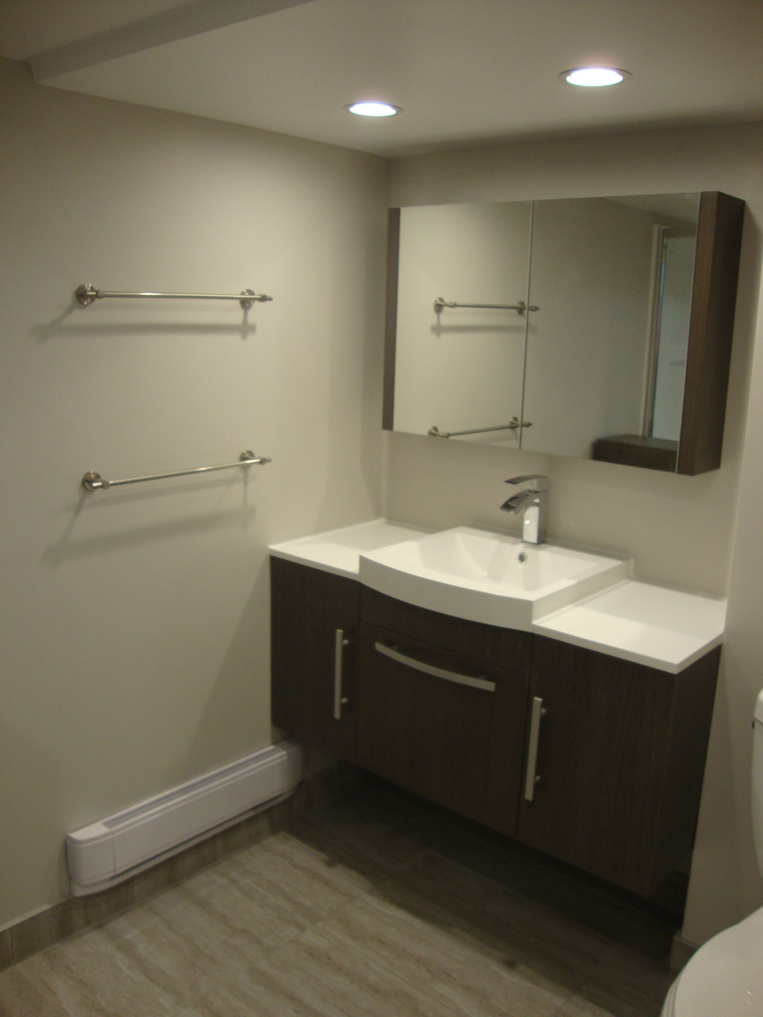 Salle de bains avec meuble-lavabo en bois foncé, comptoir blanc, lavabo carré et grand miroir.