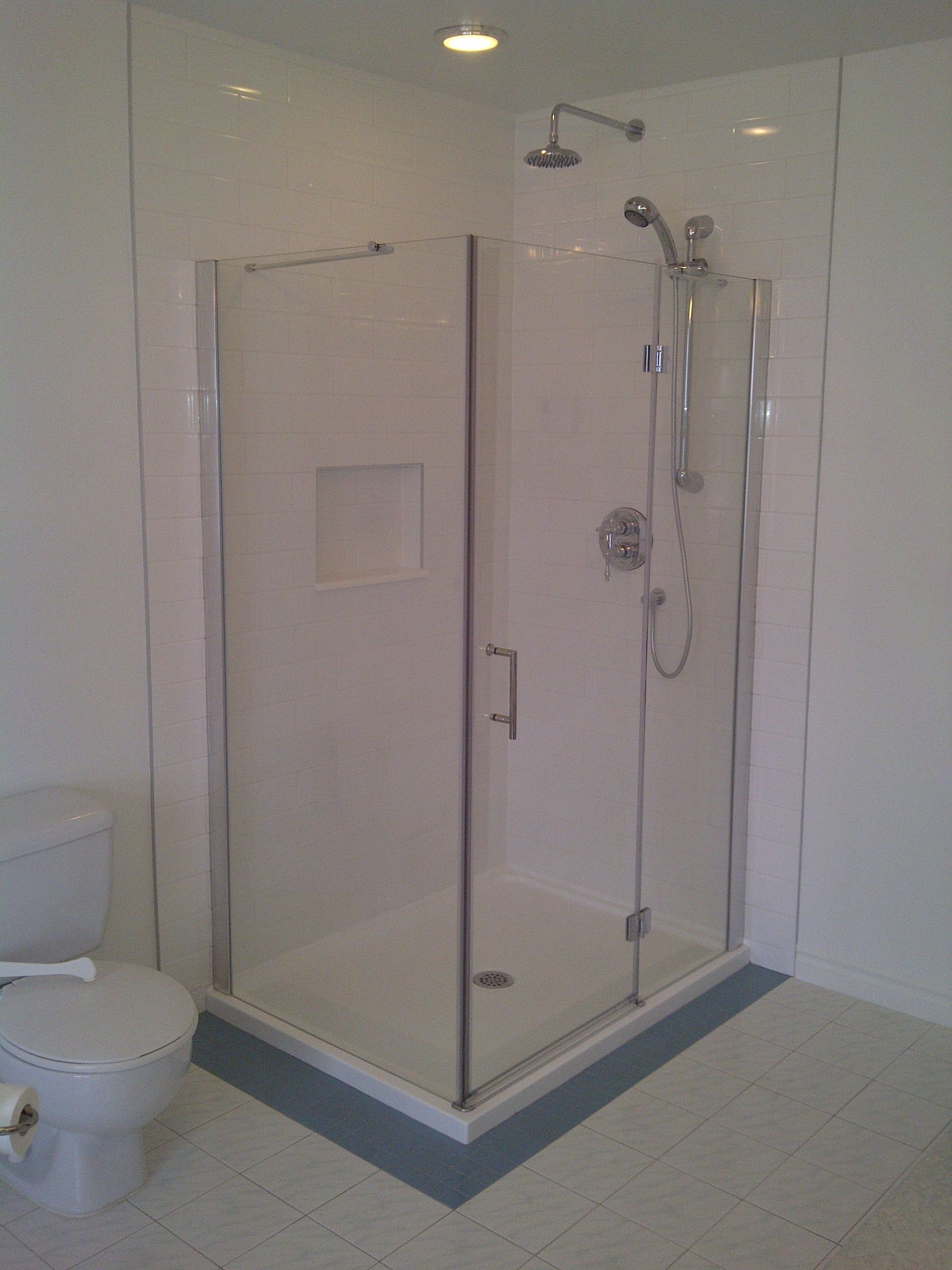 Douche d'angle avec portes en verre, robinetterie argentée et niche à savon encastrée, murs et sol carrelés.