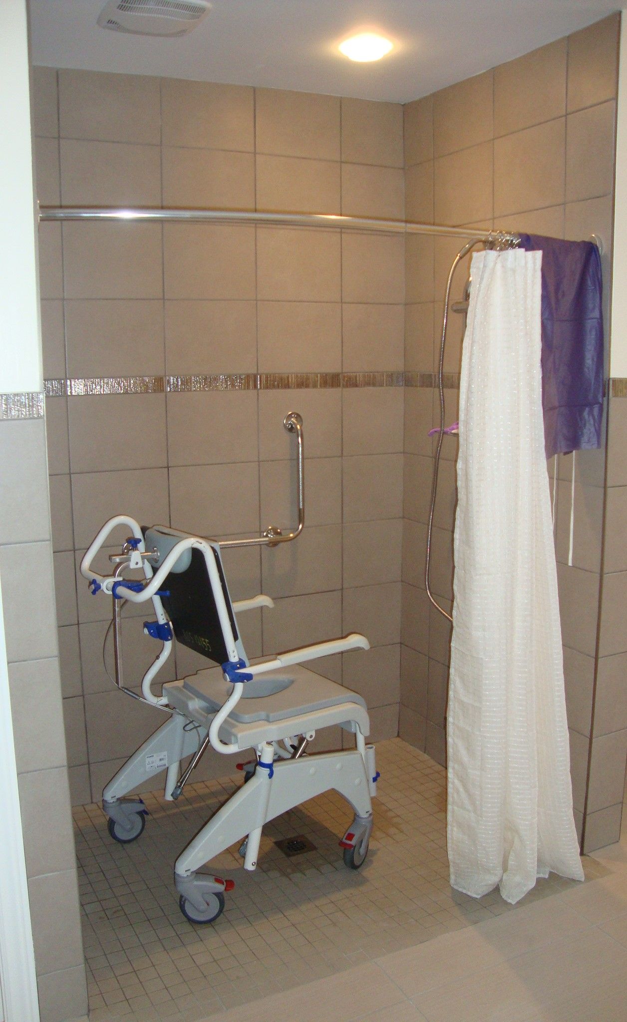 Cabine de douche accessible aux personnes en fauteuil roulant, avec siège de douche, rideau et barre d'appui.