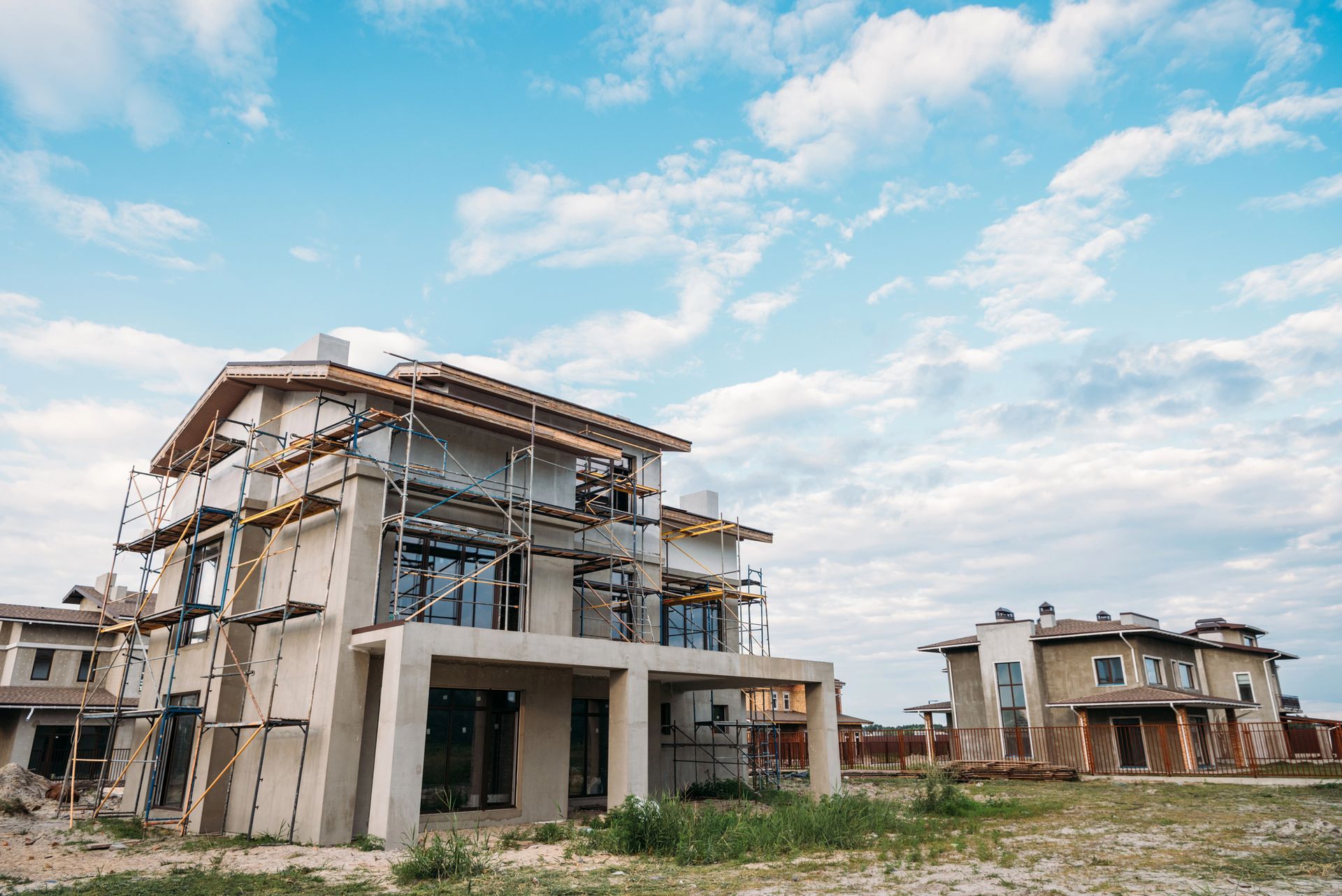 Cantiere con gru gialla che solleva materiali verso un edificio in cemento in costruzione sotto un cielo parzialmente nuvoloso.