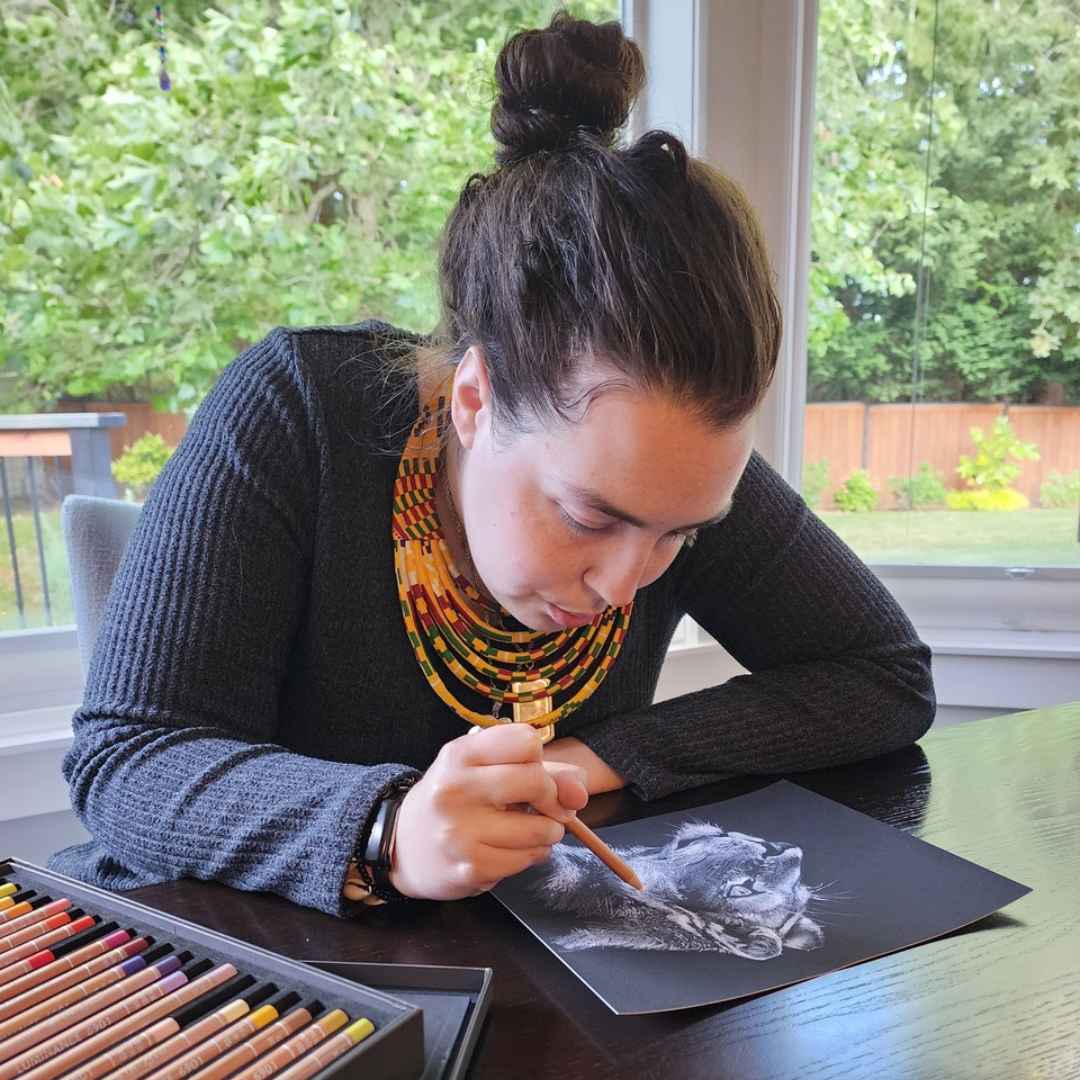 A woman is sitting at a table drawing with colored pencils.