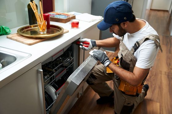 A man is fixing a dishwasher in a kitchen.