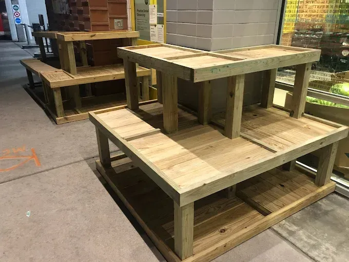 Wooden tiered display stands in a store setting. Three stands are set up with varying levels and sizes, likely for product display.
