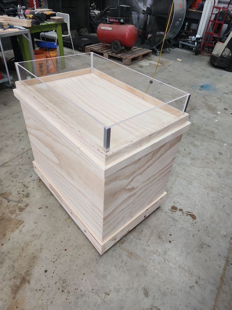 Wooden display case with a clear acrylic top and trim, in a workshop setting.