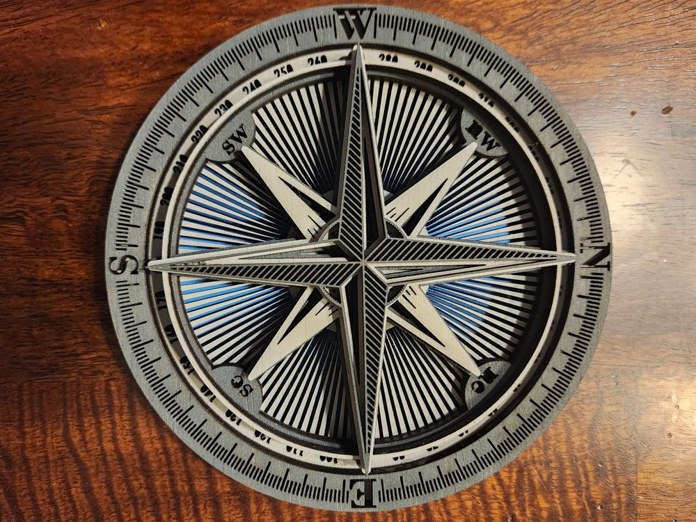 Compass rose with layered design, featuring directional markings and a starburst pattern, in gray, white, and blue.