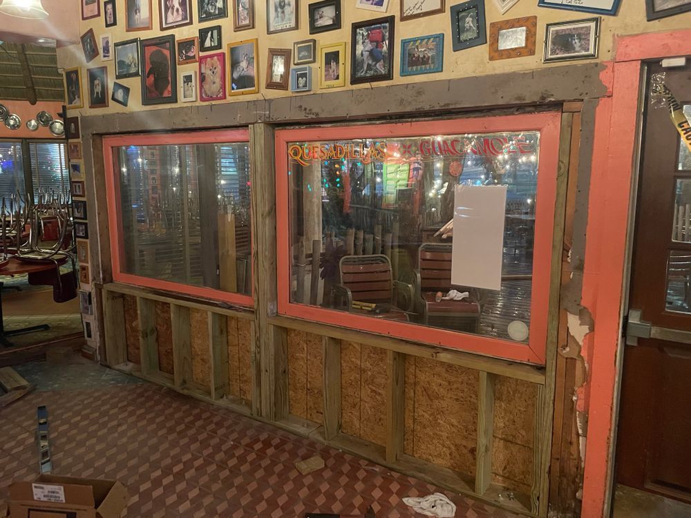 Interior view of a restaurant under construction. Two large windows with pink frames sit above exposed wooden beams and insulation.