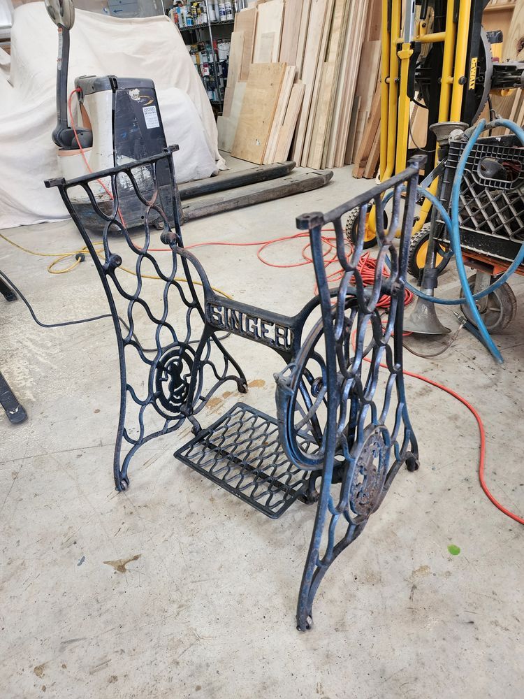 A vintage Singer sewing machine base is black, ornate metal on a concrete floor in a workshop.