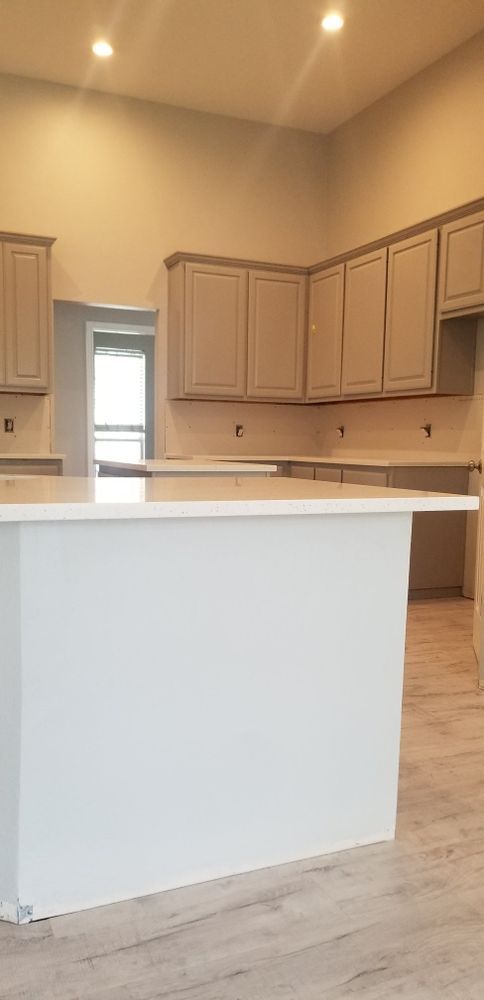 A kitchen with light gray cabinets and a white island. The walls are a light beige.