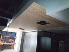 Interior under construction; wooden plank ceiling with square openings, contrasting with dark ceiling and light blue wall.