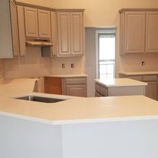 Kitchen with light gray cabinets and countertops, featuring a sink, stove hood, and island.