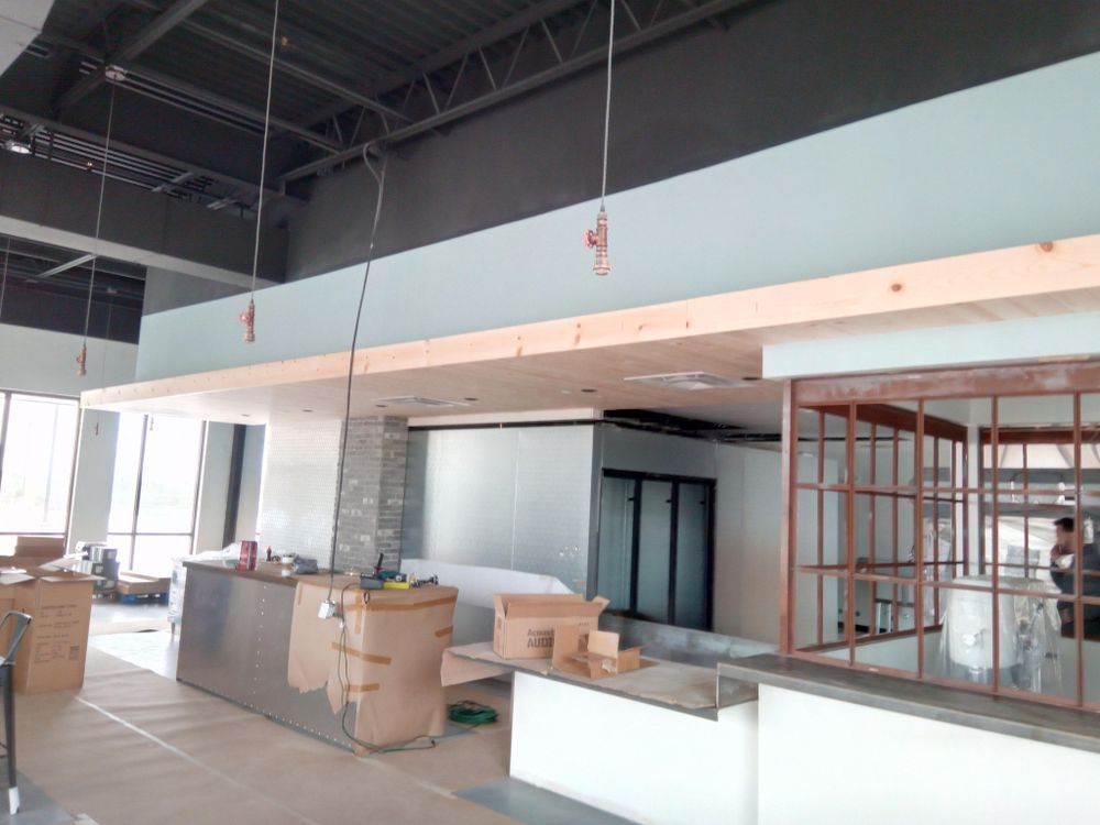 Interior construction site with unfinished bar area. A wooden beam extends across the top, and wiring hangs down.