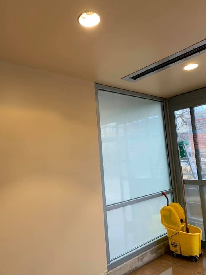 Interior view: A room with a large window covered by a white shade. A yellow mop bucket sits nearby.