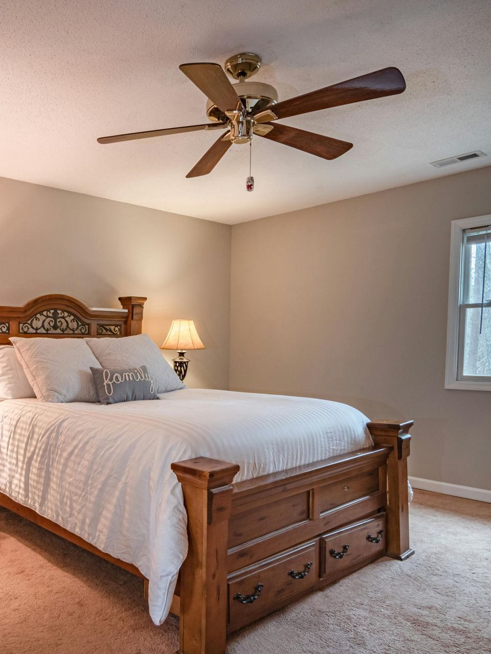 Bedroom with a wooden bed, white bedding, a bedside lamp, and a ceiling fan.