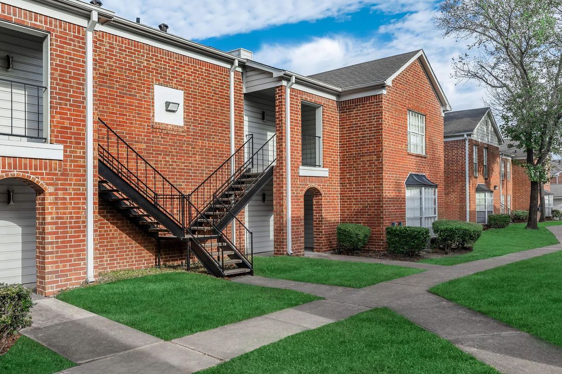 Apartment building with red brick facade, black exterior stairs, and green lawn under a blue sky.
