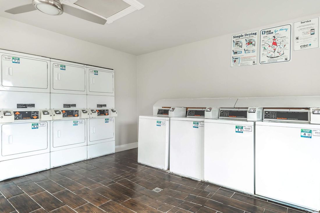 A laundry room with white washers and dryers, brown flooring, and a ceiling fan.
