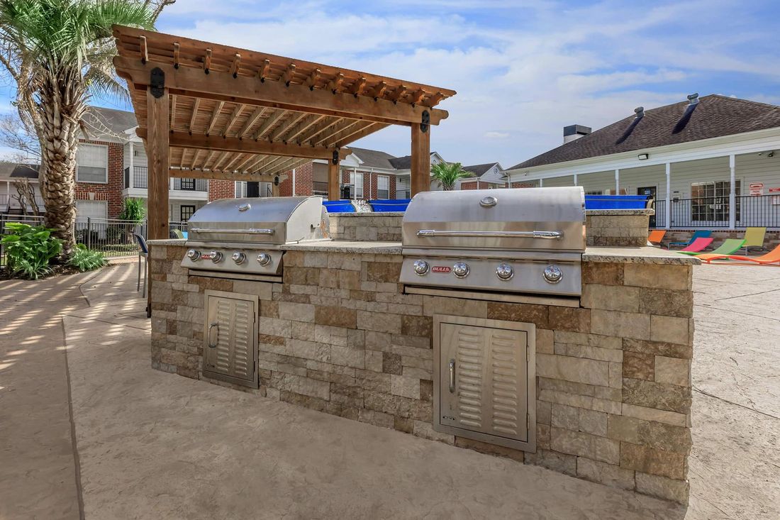 Outdoor grilling station with stone structure, two grills, and a wooden pergola.
