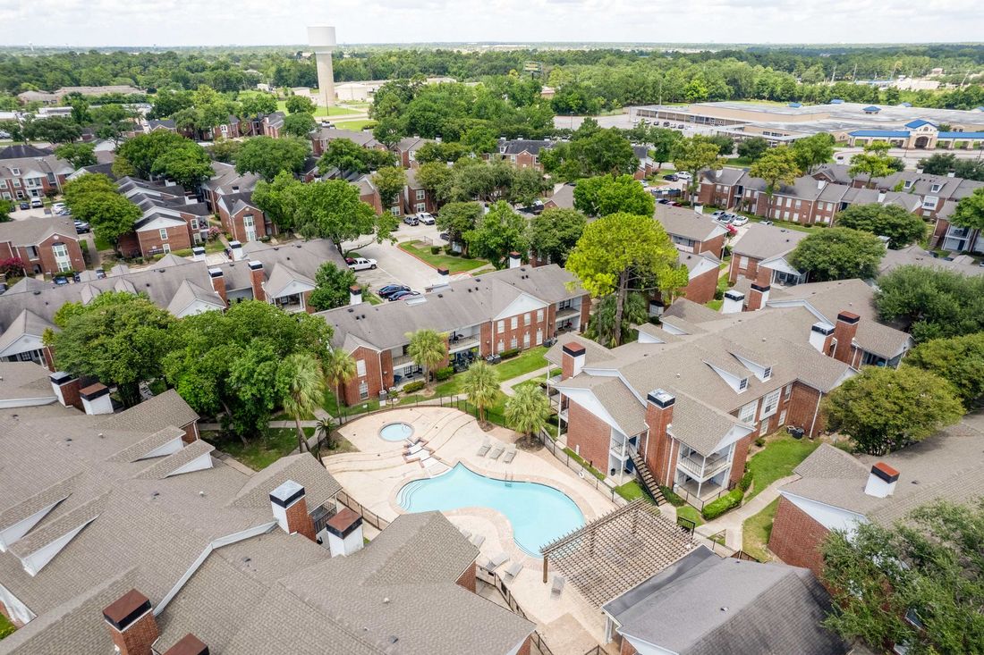 Apartment complex with a pool. Brick buildings, walkways, and a central tree.