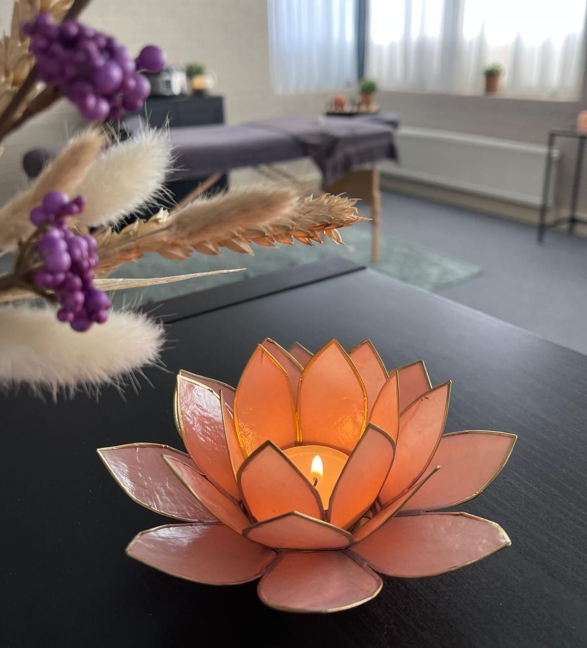 Lotus flower candle holder on a table, with a massage table in the background.