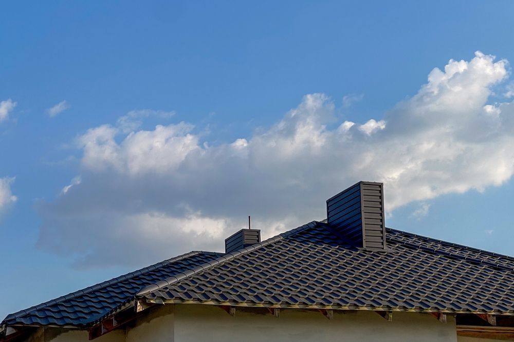 A house with a tiled roof and a chimney against a blue sky with clouds.