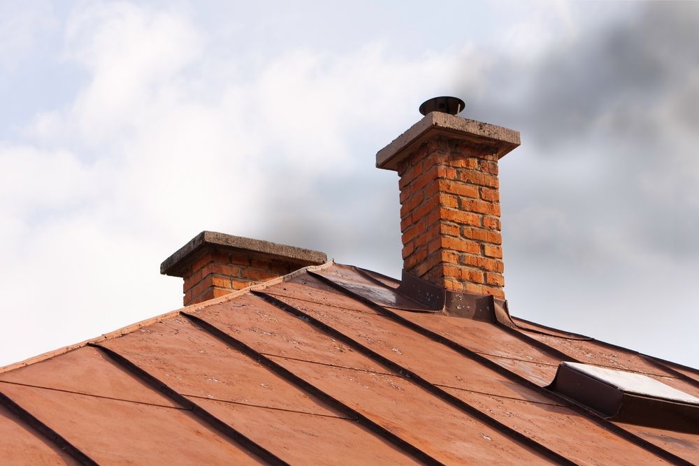 There are two chimneys on the roof of a house.