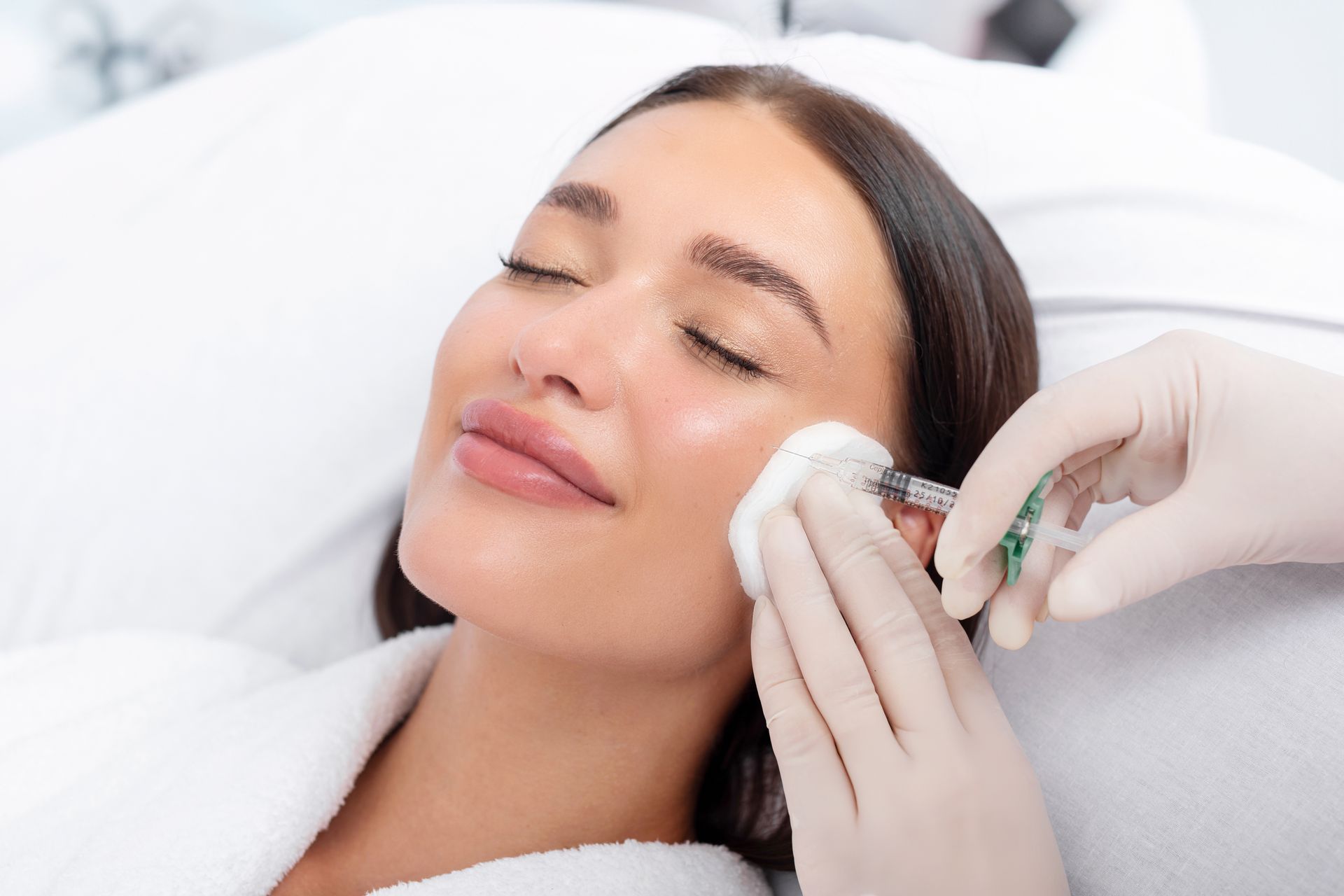 Woman receiving facial injection from gloved hand in a spa setting.