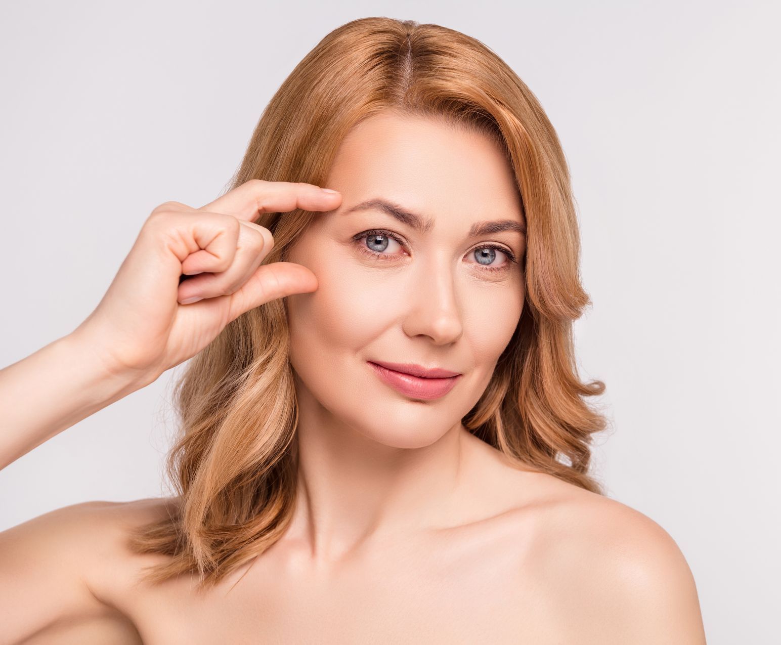 A woman is pointing at her eyebrow with her finger. 