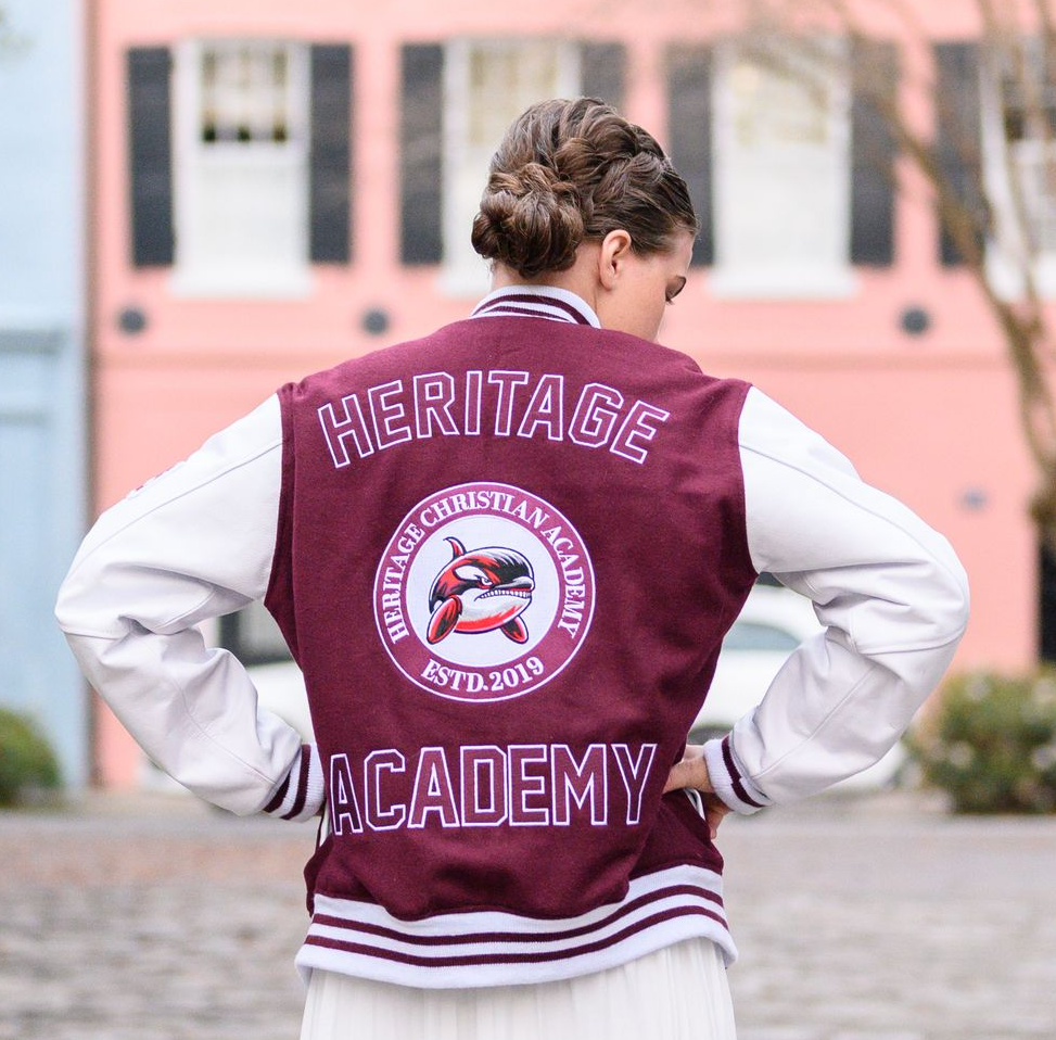 Person in maroon and white letterman jacket, Heritage Christian Academy, outdoors.