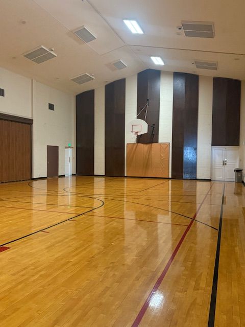 Empty gymnasium with hardwood floor, basketball hoop, and brown/white paneling.
