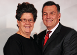 Woman with glasses and man in suit smiling together.