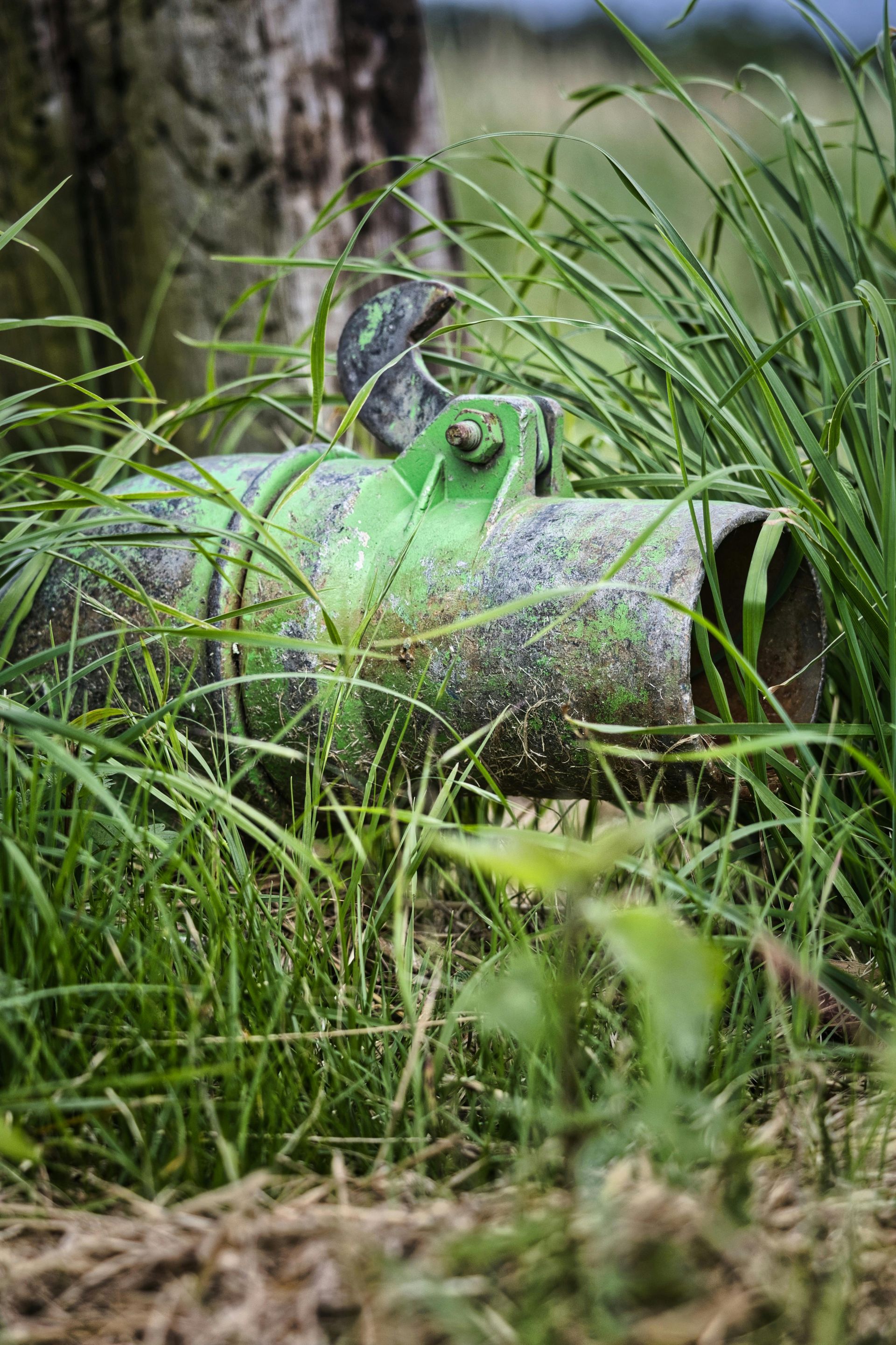 Green and silver metal drum in tall grass next to a wooden post.