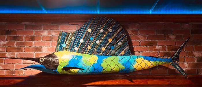 Painted sailfish decoration mounted on a brick wall with blue and green colors.