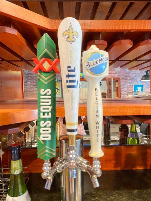 Three beer taps: Dos Equis, Miller Lite, and Blue Moon, against a wooden bar.