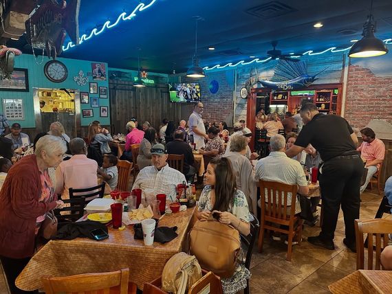 Busy restaurant interior with many people seated at tables, a server taking orders.